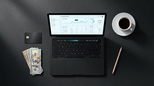 Flat lay of a laptop showing a payment dashboard, credit card, USD and AUD banknotes and a coffee cup on a charcoal surface representing the best payment processors for digital products